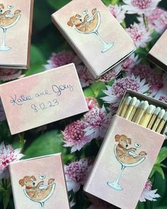 several matches are sitting on top of some pink flowers and there is a couple of cards with the names of their wedding date