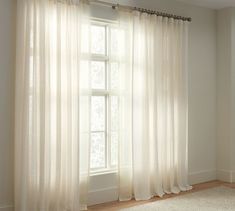 an empty room with white curtains and a window in the corner that has light coming through