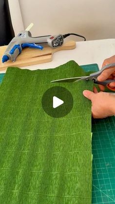 a person cutting fabric with scissors on top of a green mat and another piece of cloth in the background