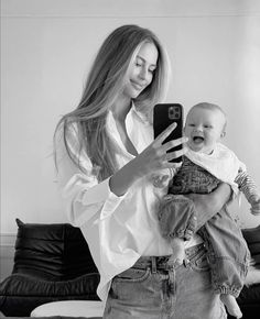 a woman is holding a baby and taking a selfie with her cell phone in the living room