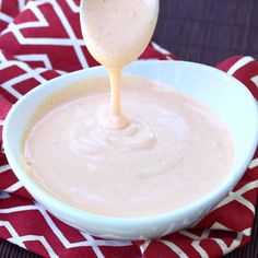 a spoon is pouring sauce into a white bowl on a red and white cloth with a red checkered napkin