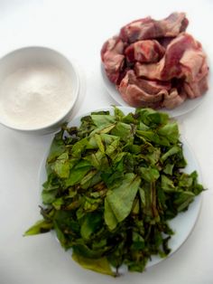 two plates filled with greens and meat next to a small bowl of ranch dressing on a white table