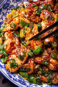 a blue and white plate topped with chicken, peppers and onions next to chopsticks