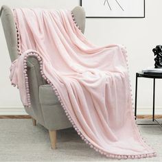 a pink blanket with pom - poms is draped over a gray chair in a living room