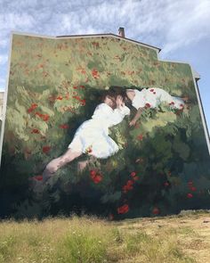 three people standing in front of a large painting on the side of a building with red flowers