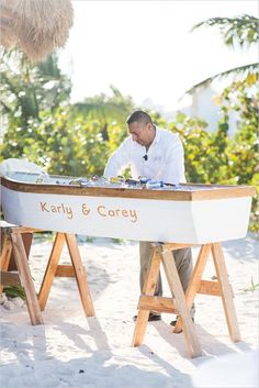 a man standing in front of a white boat on top of a sandy beach next to palm trees