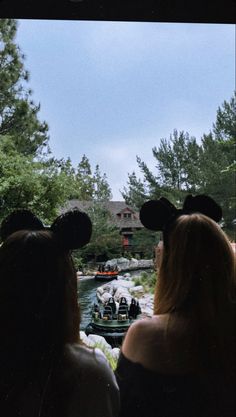 two women looking out at a boat going down the river with mickey ears on their head