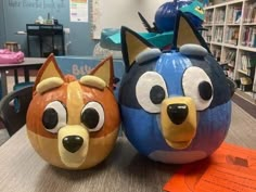 two pumpkins decorated to look like cartoon characters sitting on a table in a library