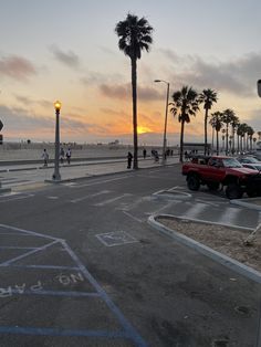 a red truck parked on the side of a road next to palm trees at sunset