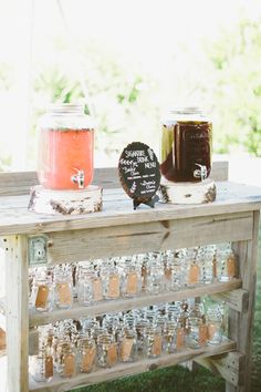 a wooden table topped with lots of jars filled with liquid next to a chalkboard sign