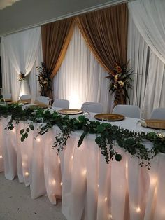 the table is set up with white linens and greenery