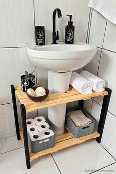 a white sink sitting next to a wooden shelf filled with towels and toiletries on top of a tiled floor