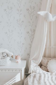 a white bed sitting under a canopy next to a wallpaper covered in pink flowers