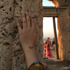 a person's hand on the side of a stone wall with people in the background