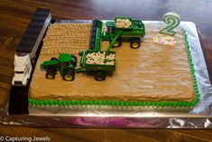 a cake with two tractors on it sitting on top of a wooden table in front of a number 2 sign