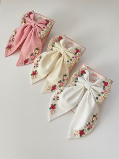 three different types of bow ties with flowers and pearls on the sides, one in pink, one in white