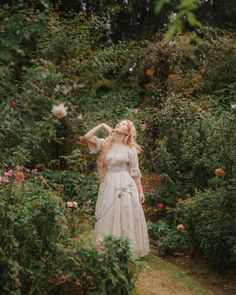 a woman in a white dress is walking through some bushes and flowers with her hair blowing in the wind