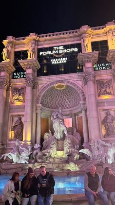 some people are standing in front of a building with fountains and statues on the sides