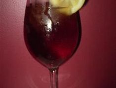 a glass filled with liquid and a lemon wedge on the rim, next to a red wall