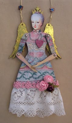 a doll is hanging on the wall with two angel wings and a flower in her hand