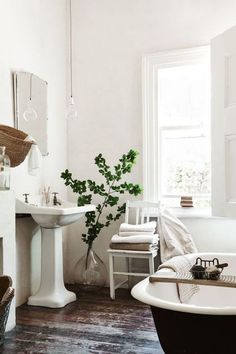 a bathroom with a tub, sink and mirror next to a plant in a vase