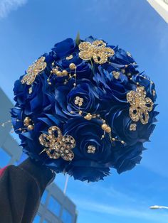 a bridal bouquet with blue flowers and gold brooches is held up in the air