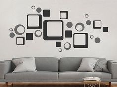 a living room with a gray couch and black wall decal on the wall above it