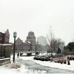 a person walking down a snow covered street in front of a large building with a clock tower