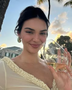 a woman holding a wine glass in front of her face and palm trees behind her