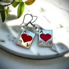 pair of earrings with red heart and ace playing card on white marble table next to plant