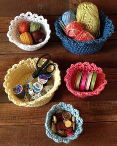 crocheted bowls with yarn and scissors in them on a wooden table next to balls of thread