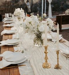 a long table with white flowers and candles on it is set for an outdoor dinner