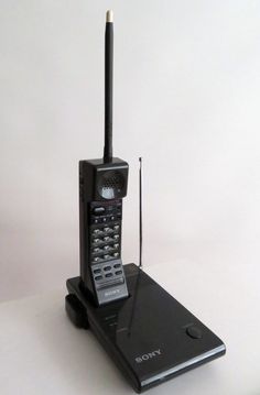 an old style cell phone sitting on top of a laptop computer with a remote control attached to it