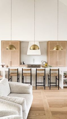 a living room and kitchen area with white walls, wood flooring and pendant lights hanging from the ceiling