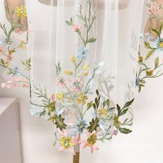 the sheer curtains are decorated with flowers and leaves in pastel colors, hanging from a metal rod