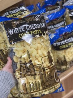 a bag of white cheddar corn puffs being held by a person's hand