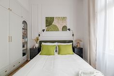 a bed with white sheets and green pillows in a bedroom next to a painting on the wall