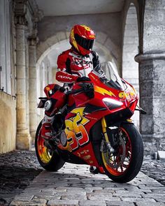 a man riding on the back of a red motorcycle down a cobblestone road