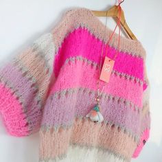 a pink and white sweater hanging on a wooden hanger with a tag attached to it