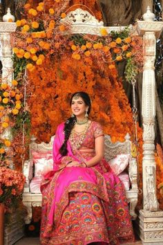 a woman sitting on top of a white bed covered in orange and pink flowers next to a tree