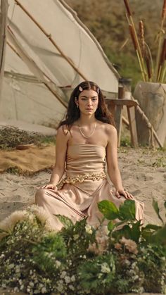 a woman sitting in the sand with flowers around her