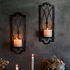 two wall sconces with lit candles on them in front of a gray wall