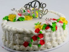 a cake with white frosting decorated with flowers and a metal monogram on top