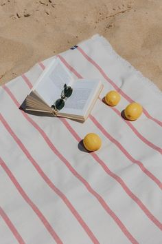 an open book sitting on top of a beach towel next to lemons and sunglasses