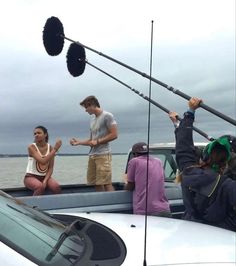 some people are sitting on a boat and one is holding up two fishing rods while the other man stands behind them