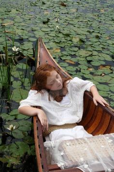 a woman in a white dress is sitting in a boat with lily pads on the water