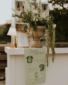 a tall vase filled with white flowers sitting on top of a table next to a sign