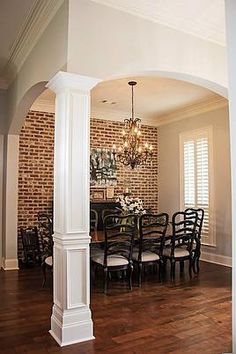 a dining room table with chairs and a chandelier hanging from the ceiling in front of a brick wall