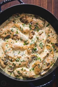 a skillet filled with chicken and mushrooms covered in gravy on top of a wooden table