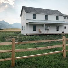 a large white house sitting on top of a lush green field next to a wooden fence